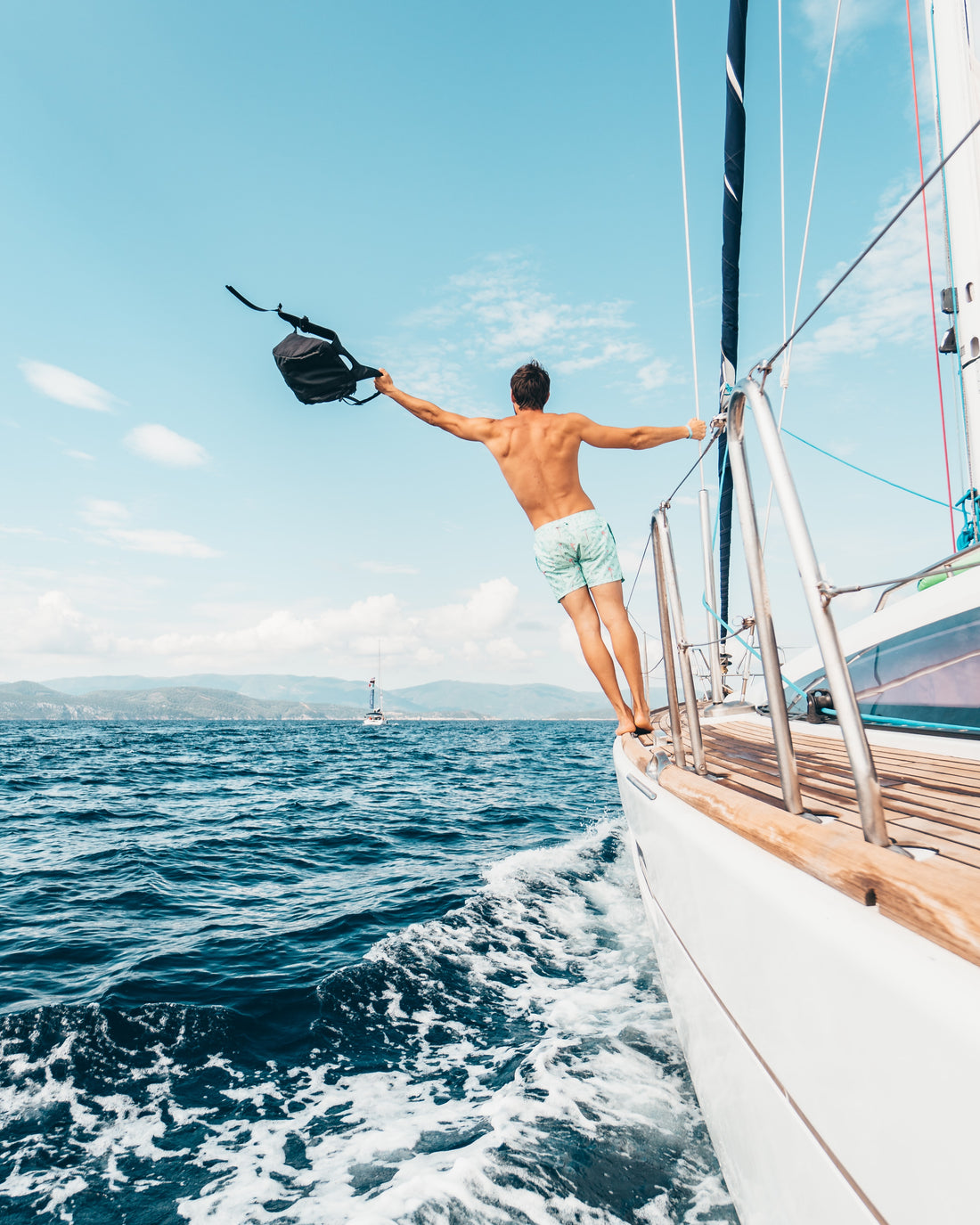 Man traveling on a sailboat waving his hat 